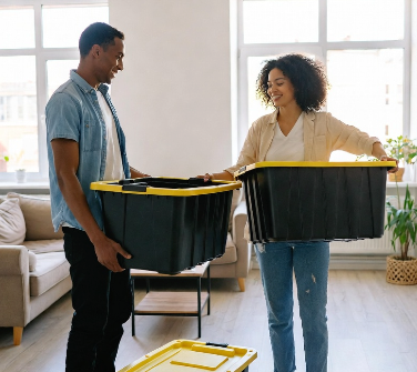 Couple happily packing belongings into black moving totes in their apartment